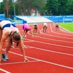 Female athletes readying to race each other on a synthetic running track.