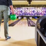 A man holding a green bowling bowl, about to make his shot in a bowling lane.