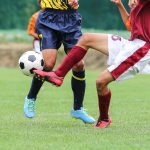 Soccer players in action on a grassy field during a daytime match.