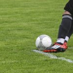 A left-footed soccer player kicking the ball on the grassy field during a match.
