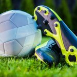 A pair of blue and yellow soccer cleats with a soccer ball next to it.
